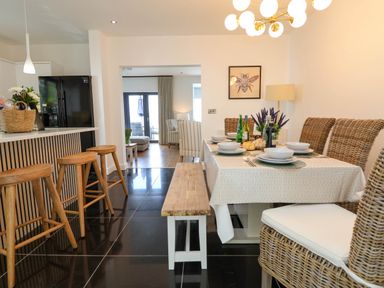 A dining area with a table set with dishes and bottles next to a kitchen island with wooden stools at Buzzards View in Dyserth