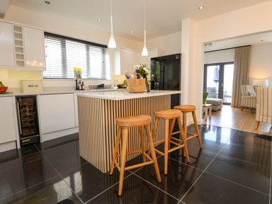 A kitchen with a central island and three wooden stools with a living room visible through an open doorway at Buzzards View in Dyserth