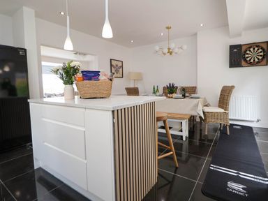 A kitchen and dining area with a white island, wicker chairs, dining table, dartboard on wall and black floor mat at Buzzards View in Dyserth