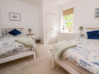 A bedroom with two single beds two bedside tables a chest of drawers and a window at Buzzards View in Dyserth