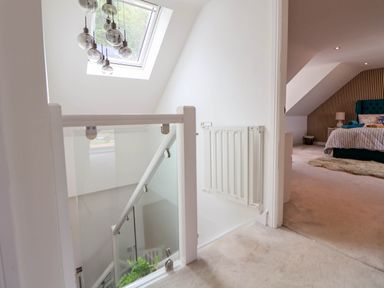 A stairwell with glass railing and a skylight next to a bedroom with a bed and side table at Buzzards View in Dyserth