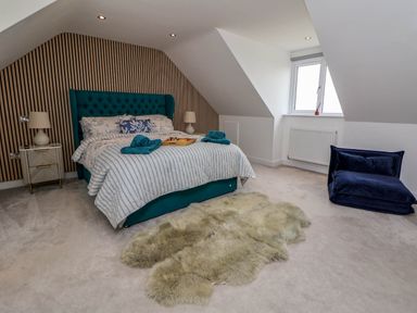A bedroom with a bed with striped bedding two nightstands with lamps a sheepskin rug and a window at Buzzards View in Dyserth