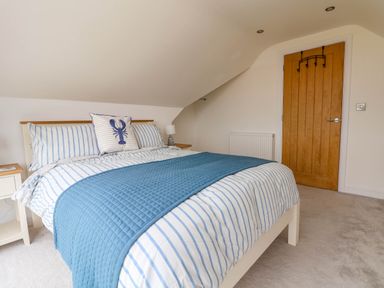 A bedroom with a bed with blue and white striped bedding and a wooden door at Buzzards View in Dyserth