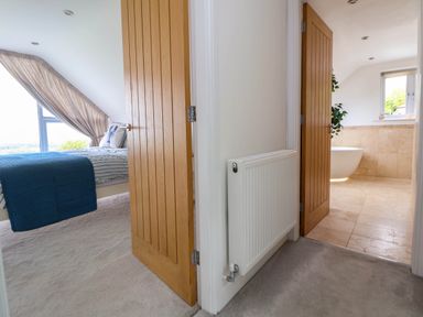 A view of a hallway with two open wooden doors leading to a bedroom with a bed and a bathroom with a bathtub at Buzzards View in Dyserth