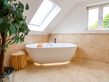 A bathroom with a freestanding bathtub under a skylight next to a wooden stool and a plant at Buzzards View in Dyserth