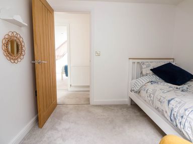 A bedroom with a bed and pillow near a wooden door that is open showing a hallway at Buzzards View in Dyserth