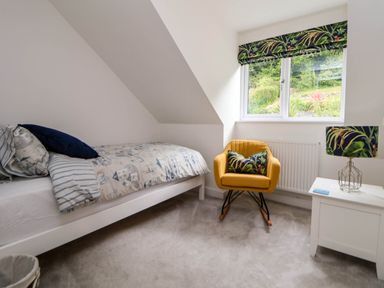 A bedroom with a single bed a yellow rocking chair a window a white bedside table and a lamp at Buzzards View in Dyserth