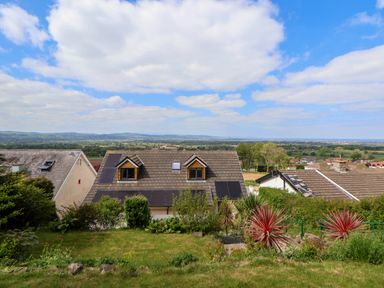 A garden with grass and plants overlooking rooftops with solar panels and a distant landscape at Buzzards View in Dyserth