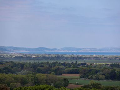 A landscape with green fields trees and hills with a body of water and distant hills at Buzzards View in Dyserth