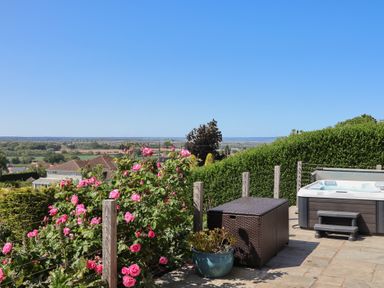 A patio with a hot tub pink flowers and garden furniture at Buzzards View in Dyserth