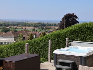 A patio area with a hot tub and outdoor furniture overlooking houses fields and the sea at Buzzards View in Dyserth