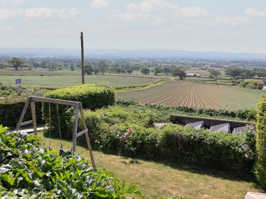 A garden with a wooden swing set and a view of farmland and solar panels at Buzzards View in Dyserth