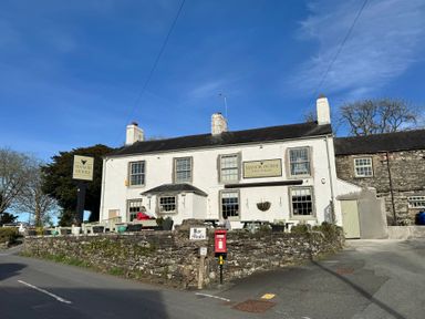 An outdoor view of a white building with signs reading Manor House and Bar Meals with a stone wall and benches at Old Cottage in Oxen Park near Ulverston