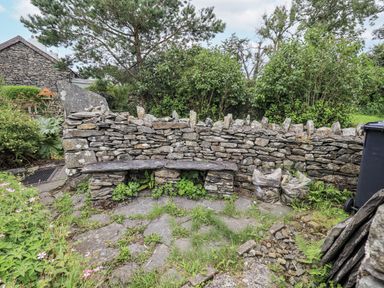 A garden area with a stone wall and wooden bench at Old Cottage in Oxen Park near Ulverston
