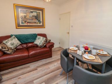A dining area with a table set for four and a leather sofa with cushions and a framed artwork on the wall at Number Ten in Amble