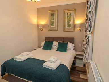 A bedroom with a double bed two pillows two bedside tables two framed pictures on the wall and folded towels on the bed at Number Ten in Amble