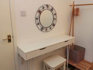 A dressing table with drawers a stool a round wall mirror with butterfly designs and a wooden clothing rack with hangers and a storage basket at Number Ten in Amble