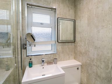A bathroom with a sink a mirror a window with blinds and a soap dispenser at Number Ten in Amble
