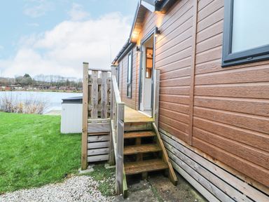 Wooden steps leading to an open door of a brown cabin near a lake with grass and gravel pathway at 12A Lake Escape in Carnforth