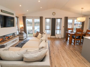 A living room with a sectional sofa a fireplace a wall-mounted TV and a dining table with chairs at 12A Lake Escape in Carnforth