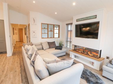 A living room with a large sectional sofa a wall-mounted television and an electric fireplace at 12A Lake Escape in Carnforth