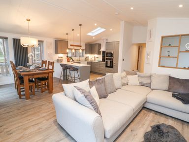 An open plan living room kitchen and dining area with a large beige sectional sofa wooden dining table with chairs and a kitchen island with stools at 12A Lake Escape in Carnforth