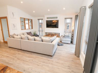 A living room with a beige sectional sofa a wall-mounted television and a fireplace at 12A Lake Escape in Carnforth