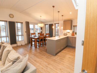 A dining area with a wooden table and chairs next to a kitchen with gray cabinets and pendant lights at 12A Lake Escape in Carnforth