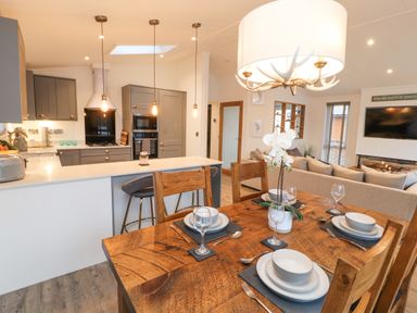 A dining area with wooden table set for four near a kitchen with grey cabinets and a living room with a beige sofa at 12A Lake Escape in Carnforth