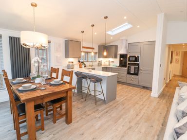 A kitchen and dining area with a wooden dining table set and a gray kitchen island with stools at 12A Lake Escape in Carnforth