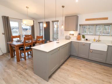A kitchen with grey cabinets a white countertop a farmhouse sink and a wooden dining table with chairs at 12A Lake Escape in Carnforth