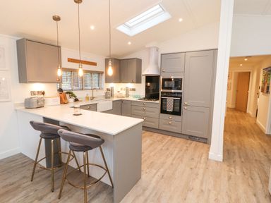 A kitchen with grey cabinets a white countertop and two bar stools at 12A Lake Escape in Carnforth