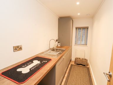 A narrow kitchen with a countertop sink and a mat that says bone appetit with pet bowls at 12A Lake Escape in Carnforth