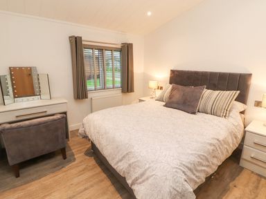 A bedroom with a bed a vanity table with a mirror and chair and windows with curtains at 12A Lake Escape in Carnforth