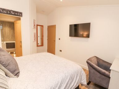 A bedroom with a bed a wall mounted TV a chair a mirror and two doors at 12A Lake Escape in Carnforth