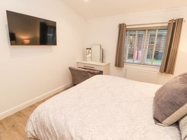 A bedroom with a bed a wall mounted TV a desk with a mirror and a window with curtains at 12A Lake Escape Carnforth