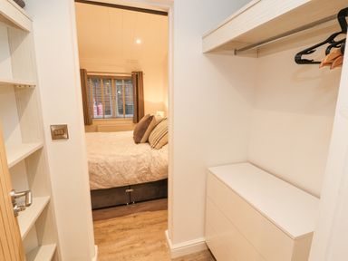A bedroom visible through a walk-in closet with hangers on a rod and a chest of drawers at 12A Lake Escape in Carnforth
