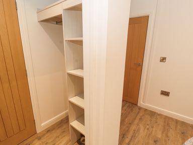 A small room with wooden shelves a hanging rod a wooden door and wooden flooring at 12A Lake Escape in Carnforth