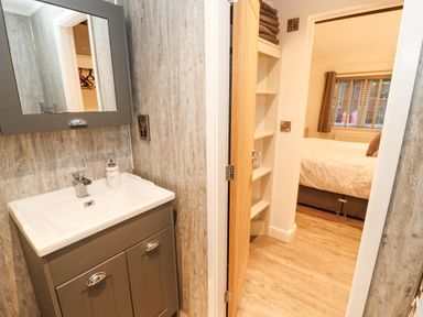 A bathroom with a sink and mirror next to a doorway leading to a bedroom with a bed and window at 12A Lake Escape Carnforth