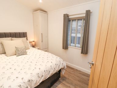 A bedroom with a bed a wardrobe a window with curtains and wooden flooring at 12A Lake Escape in Carnforth