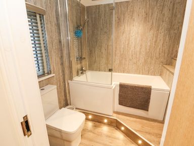A bathroom with a toilet a bathtub with shower and a towel on the side at 12A Lake Escape in Carnforth