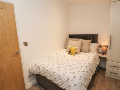 A bedroom with a bed with dog patterned bedding cushions bedside table with lamp and wooden wardrobe at 12A Lake Escape in Carnforth
