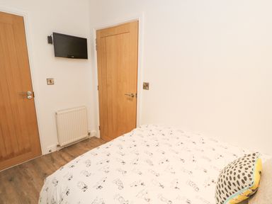 A bedroom with a bed covered in dog print bedding two wooden doors a wall-mounted TV and a radiator at 12A Lake Escape in Carnforth