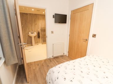 A bedroom with wooden floor a bed with printed sheets a wall mounted TV and an open door leading to a bathroom at 12A Lake Escape in Carnforth