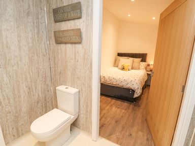 A toilet area with wood textured walls and signs next to a bedroom with a bed and pillows at 12A Lake Escape in Carnforth