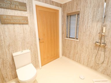 A bathroom with a toilet shower window wooden door and two wall signs at 12A Lake Escape in Carnforth