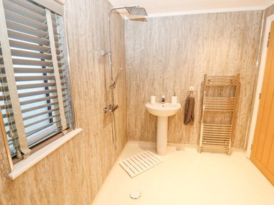 A bathroom with a shower, a pedestal sink, a towel rack, and a window at 12A Lake Escape in Carnforth