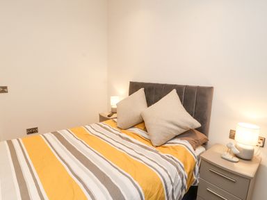 A bedroom with a bed with striped yellow and gray bedding and two beige pillows at 12A Lake Escape in Carnforth