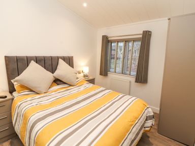 A bedroom with a double bed with striped bedding a window with curtains and a wardrobe at 12A Lake Escape in Carnforth