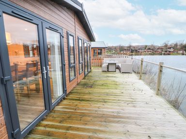 An outdoor wooden deck with glass doors, outdoor seating, and a view of a lake at 12A Lake Escape in Carnforth
